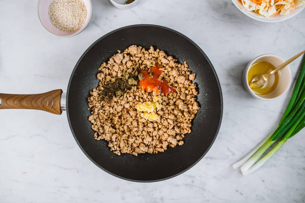Keto Egg Roll In A Bowl Adding spices into the egg roll filling inside a black pan with a wooden handle