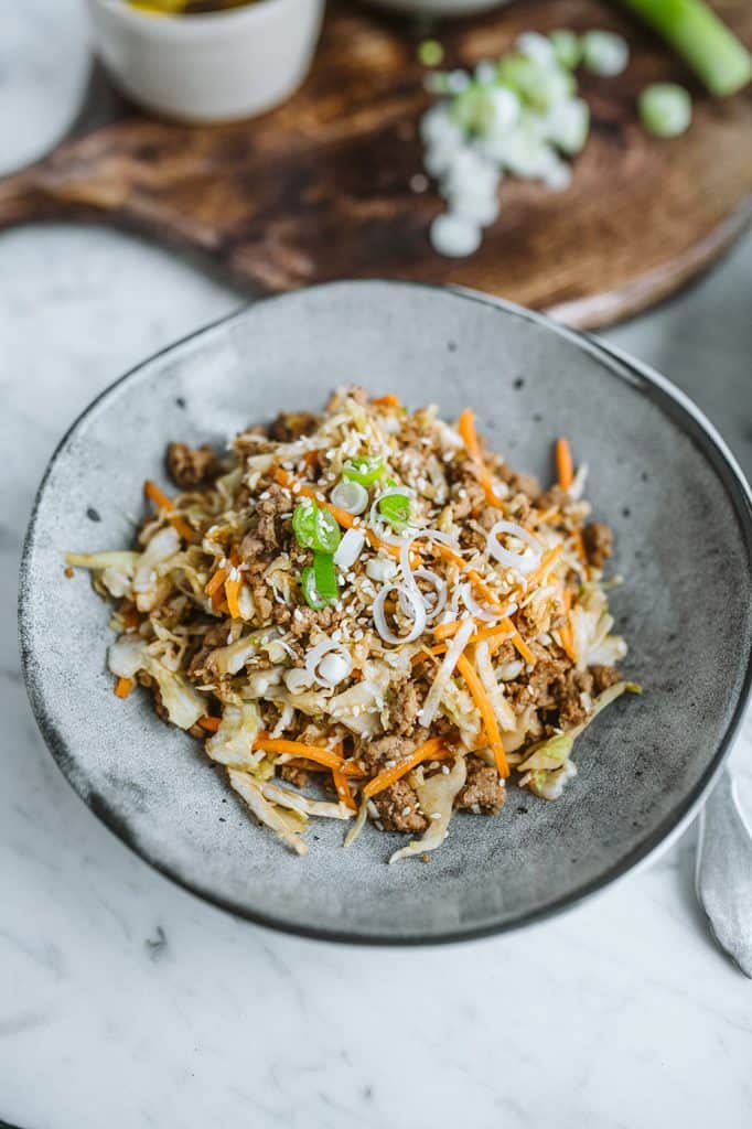 egg roll in a bowl served on a grey plate with cutting board in the background