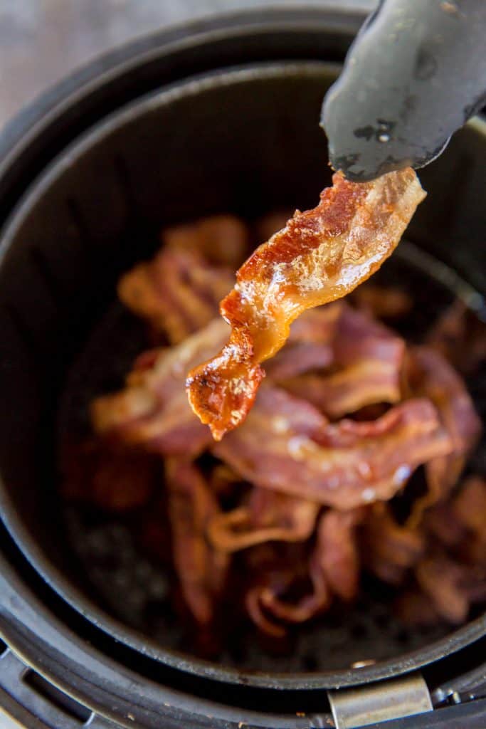 Checking the cooked bacon with tongs