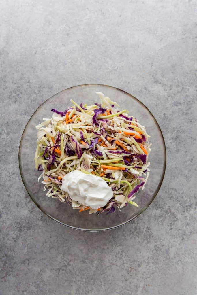 adding sour cream to the keto coleslaw in a mixing bowl