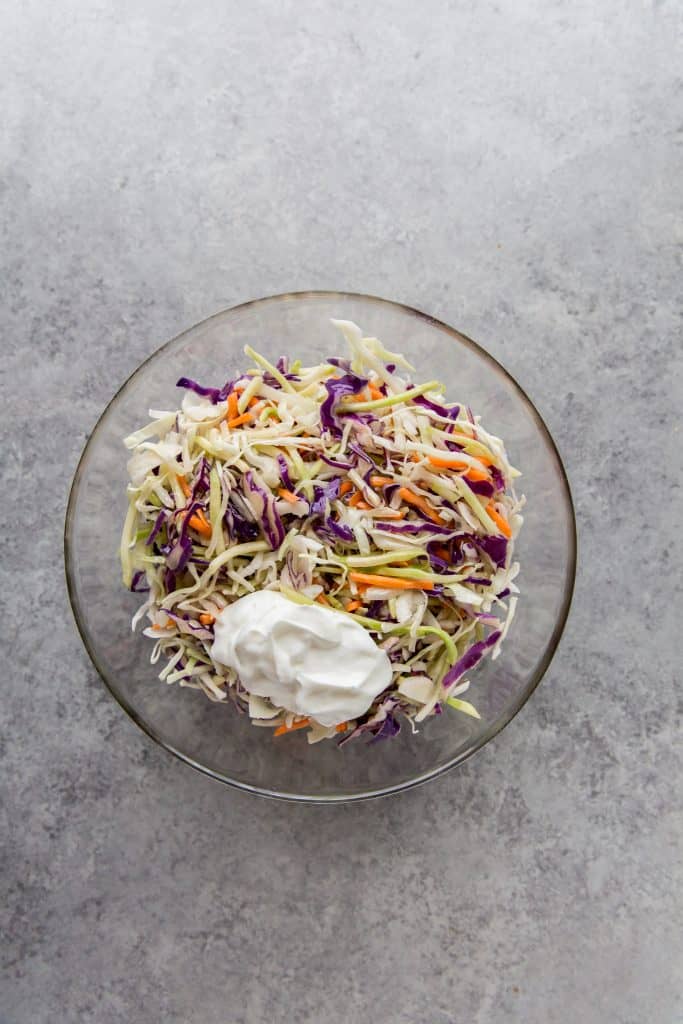 keto coleslaw adding sour cream to the keto coleslaw in a mixing bowl