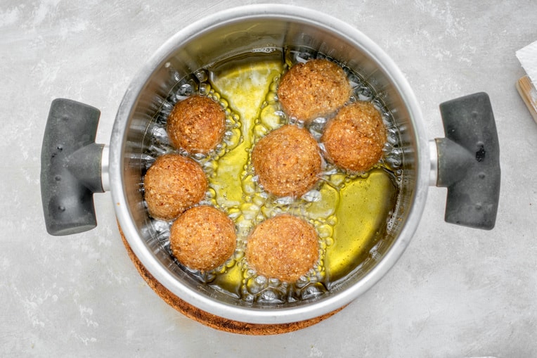 Keto donuts being fried in a metal pot with oil