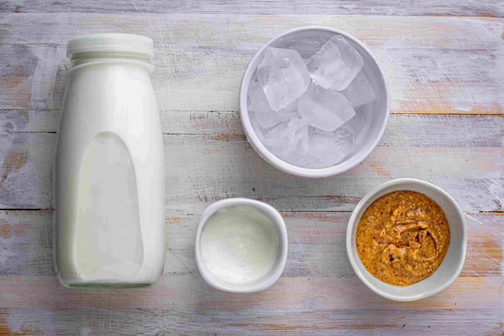 Almond butter, cream, ice, and almond milk measured in ceramic bowls. 