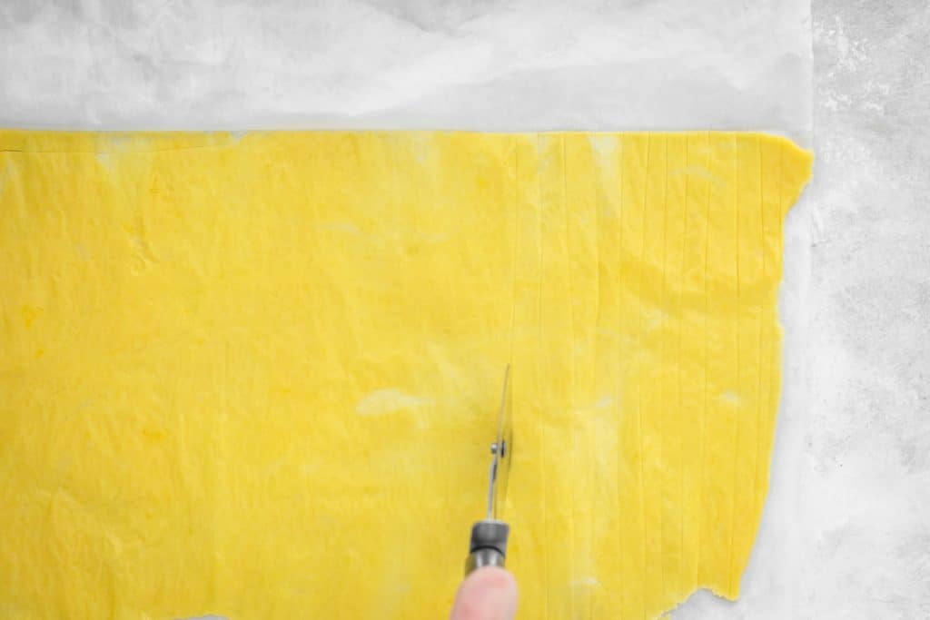 cutting through the pasta dough with a pink handled pizza cutter