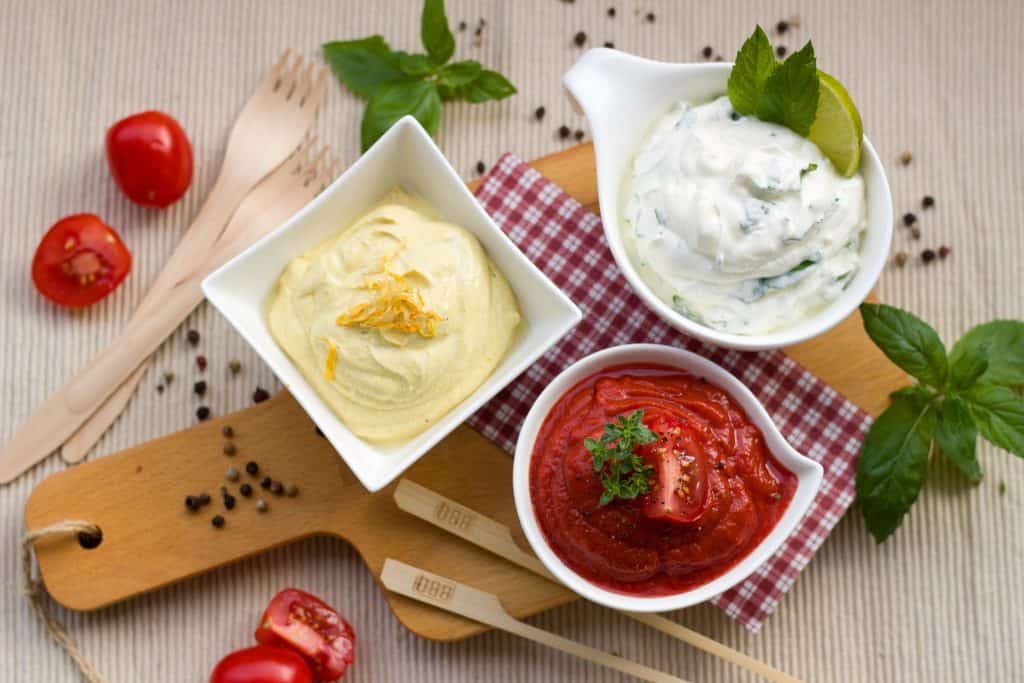 three different sauces on a cutting board with herbs