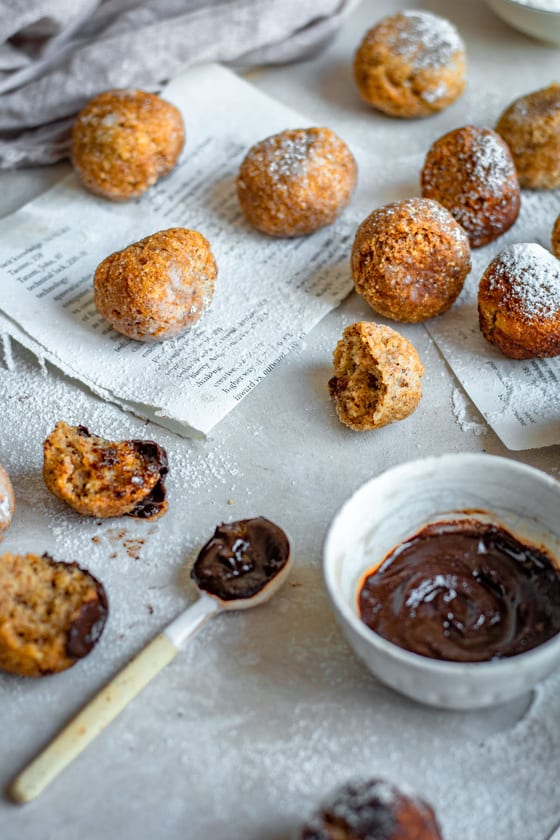 Keto Donuts A bowl of chocolate with a spoon dipped in it next to freshly fried donuts.