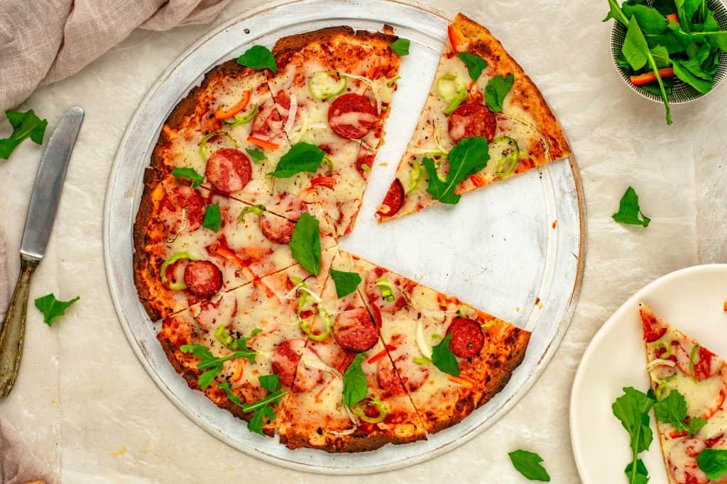 keto pizza pizza on a tray sliced with greens on top