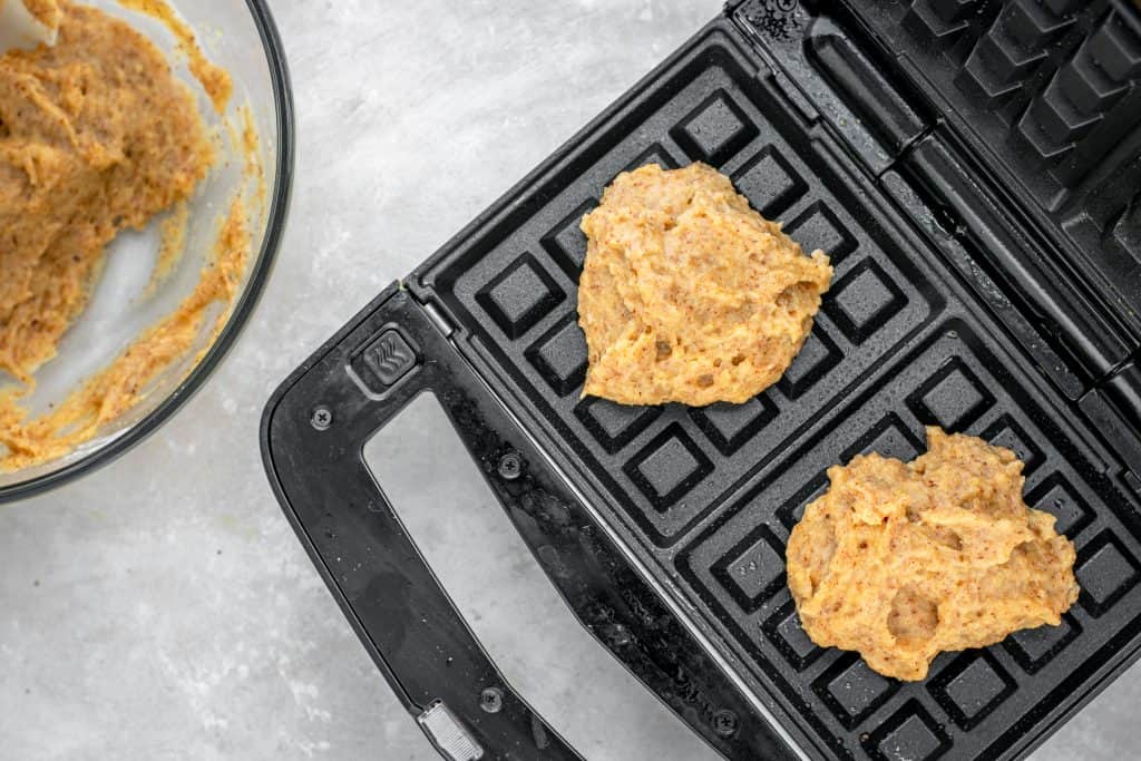 Waffle batter scooped into two square waffle maker sections