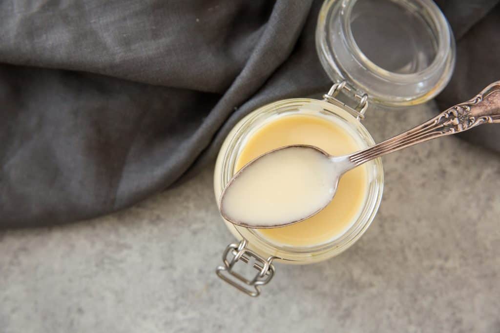 A silver spoon dipped in condensed milk resting on a glass jar