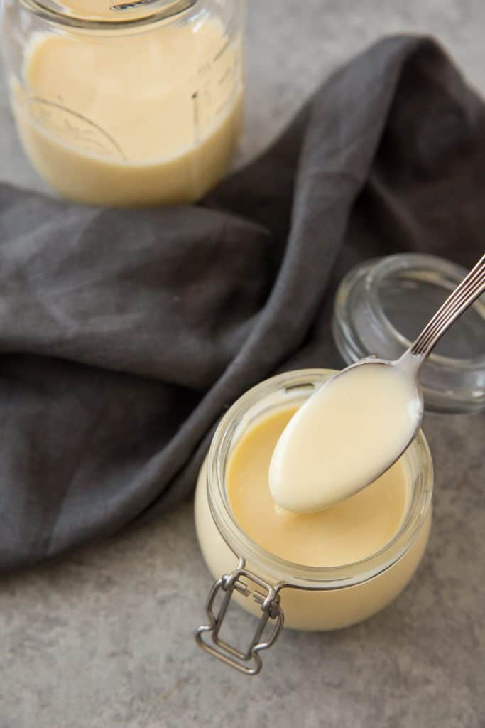 Two full jars of keto condensed milk next to a grey dish cloth. 