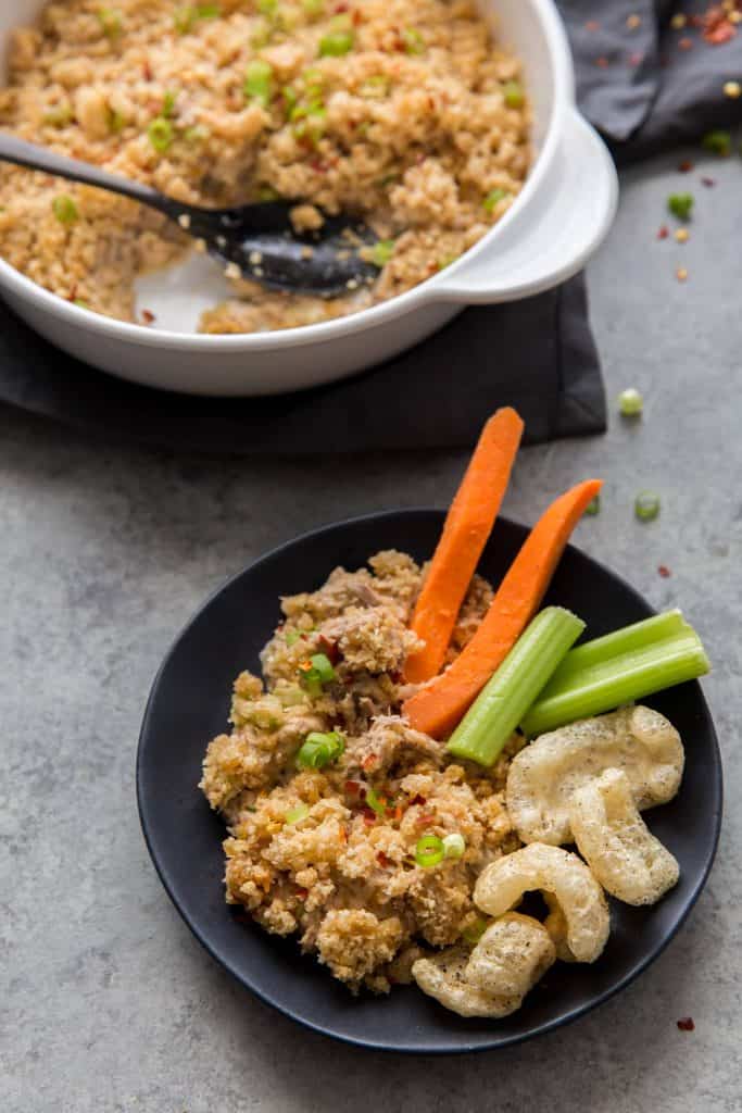 Cheesy tuna casserole on a black plate in front of a white casserole dish with leftovers. 