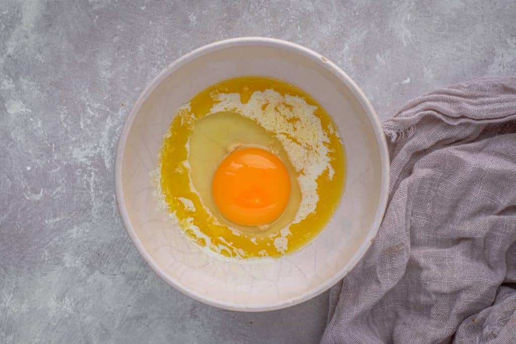 A bowl with an egg and butter next to a purple cloth