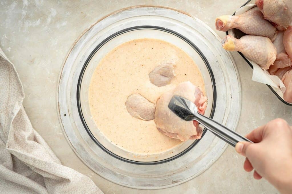 Keto Fried Chicken Using tongs to dip chicken thighs into a keto marinade