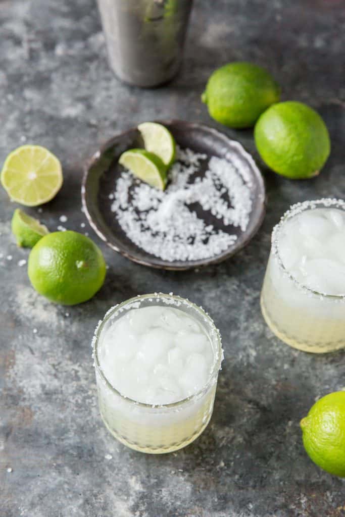 Two completed margaritas in front of a plate with salt and lime wedges.