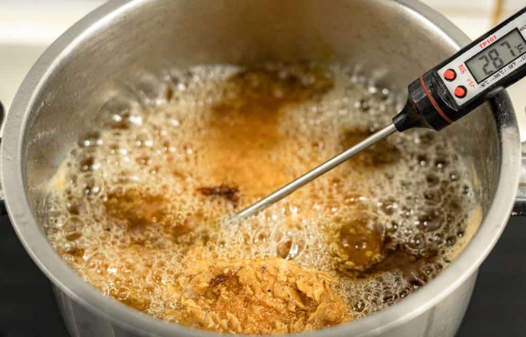 A thermometer checking the chicken temp while frying 