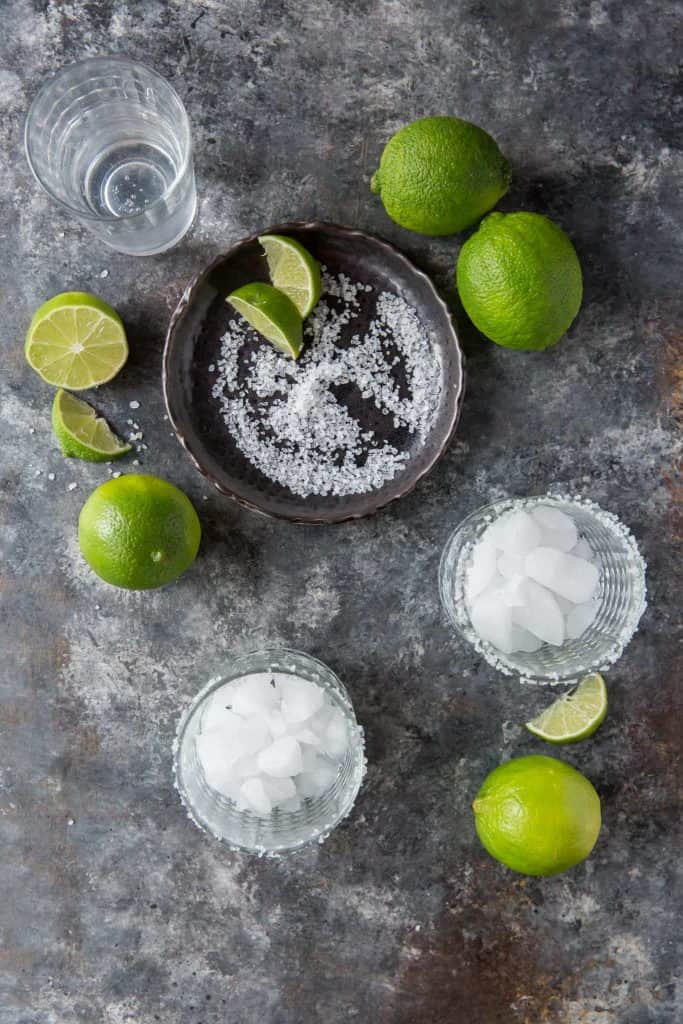 Margarita glasses with salt and ice next to fresh limes