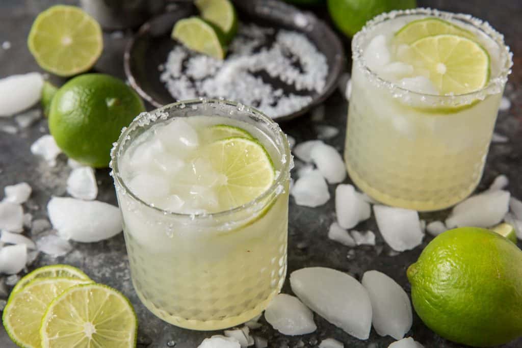 Prepared keto margaritas next to crushed ice and lime.