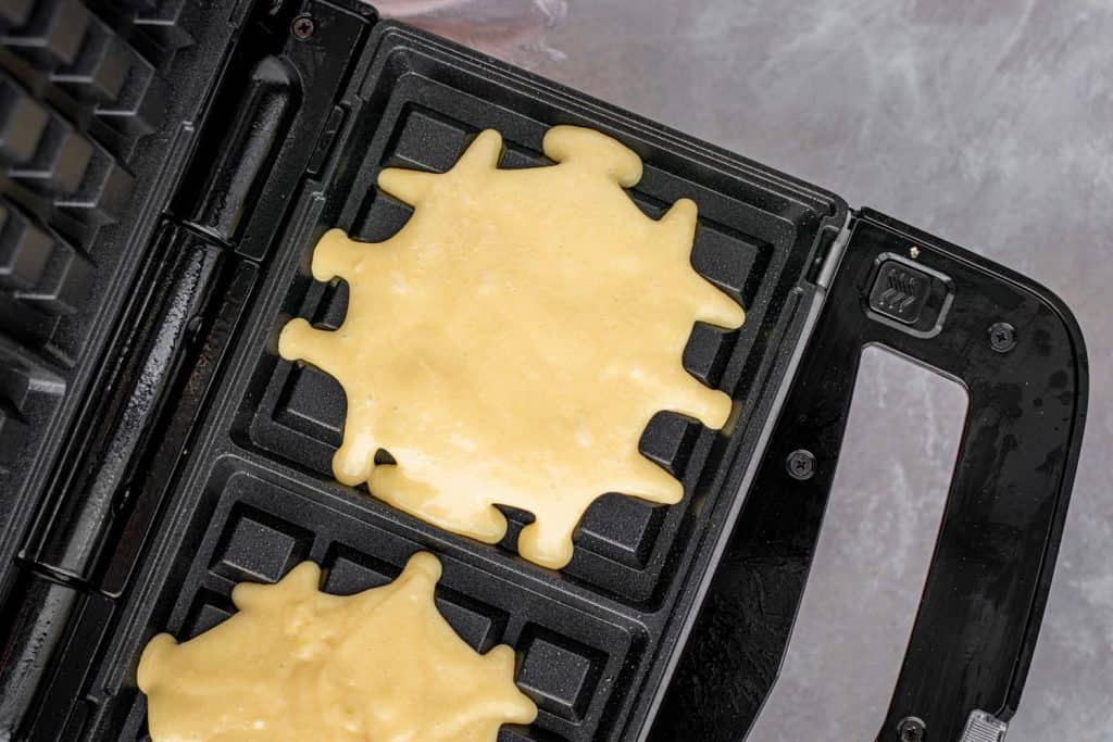 A waffle iron heating with two servings of raw batter to make waffles.