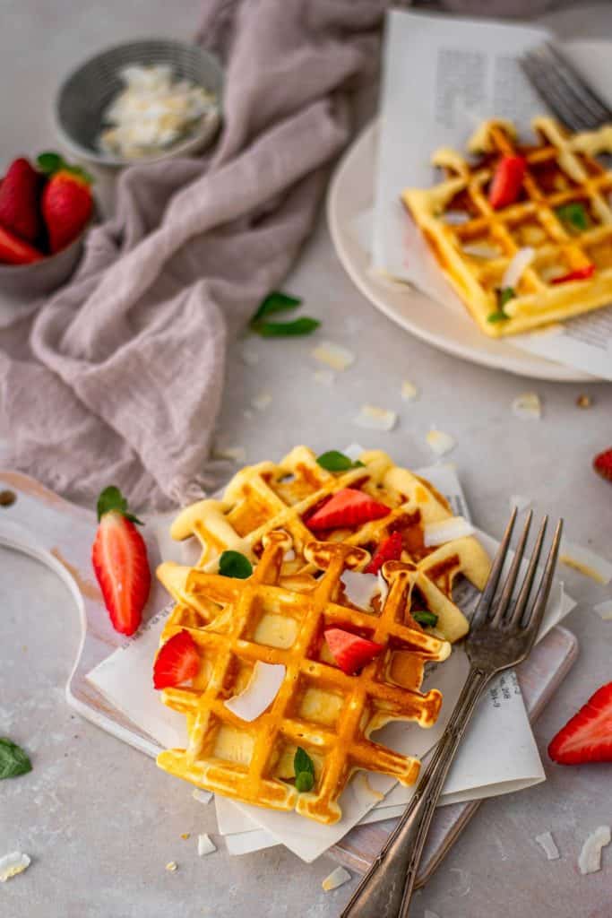 Two protein waffles on a cutting board topped with strawberries and mint. 