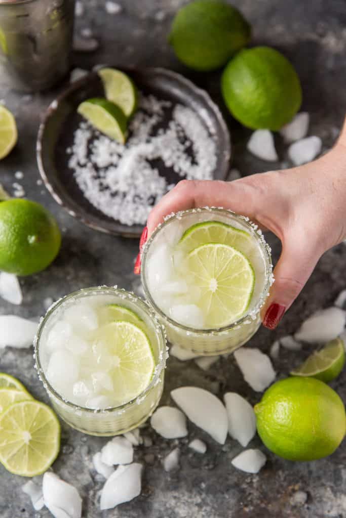 Keto Margarita Someone holding a cold keto margarita and clinking glasses.