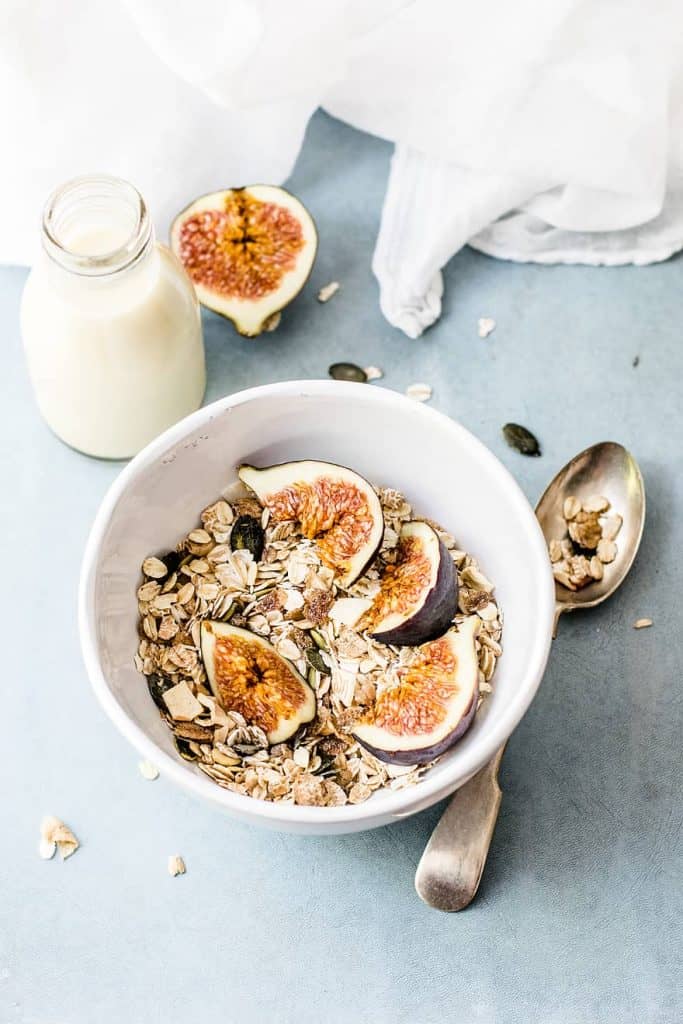 A bowl of granola next to milk and a silver spoon