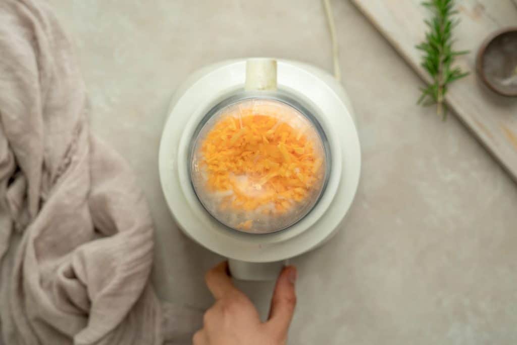 Cheese being mixed to form a dough with a hand grasping the food processor