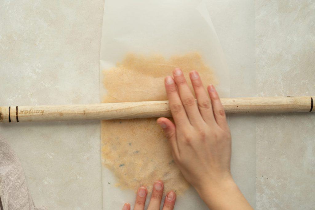 A wooden dowel being used to roll out herb cracker dough