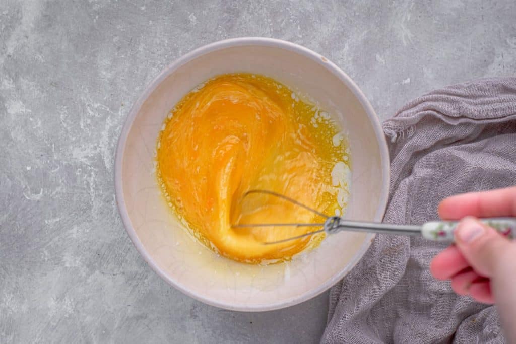 whisking eggs and butter together until combined in a ceramic mixing bowl