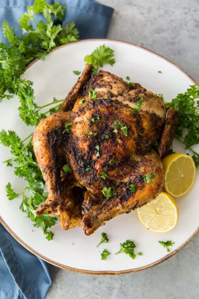 A whole roasted chicken on a bed of parsley with a whole lemon
