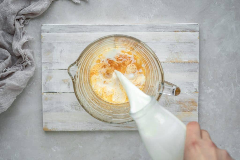 A white wooden board with a glass measuring cup and custard ingredients