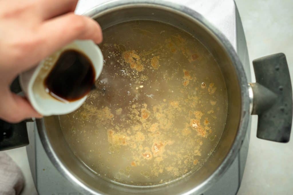 Keto Egg Drop Soup hand mixing spices and soy sauce into chicken broth