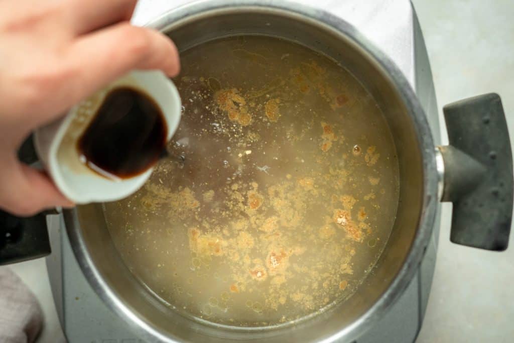 hand mixing spices and soy sauce into chicken broth