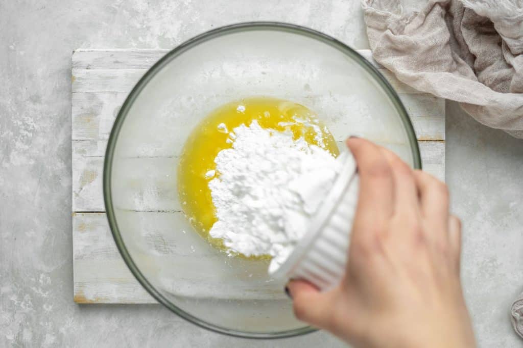 keto peanut butter fudge powdered sweetener being sprinkled into a glass bowl of melted butter