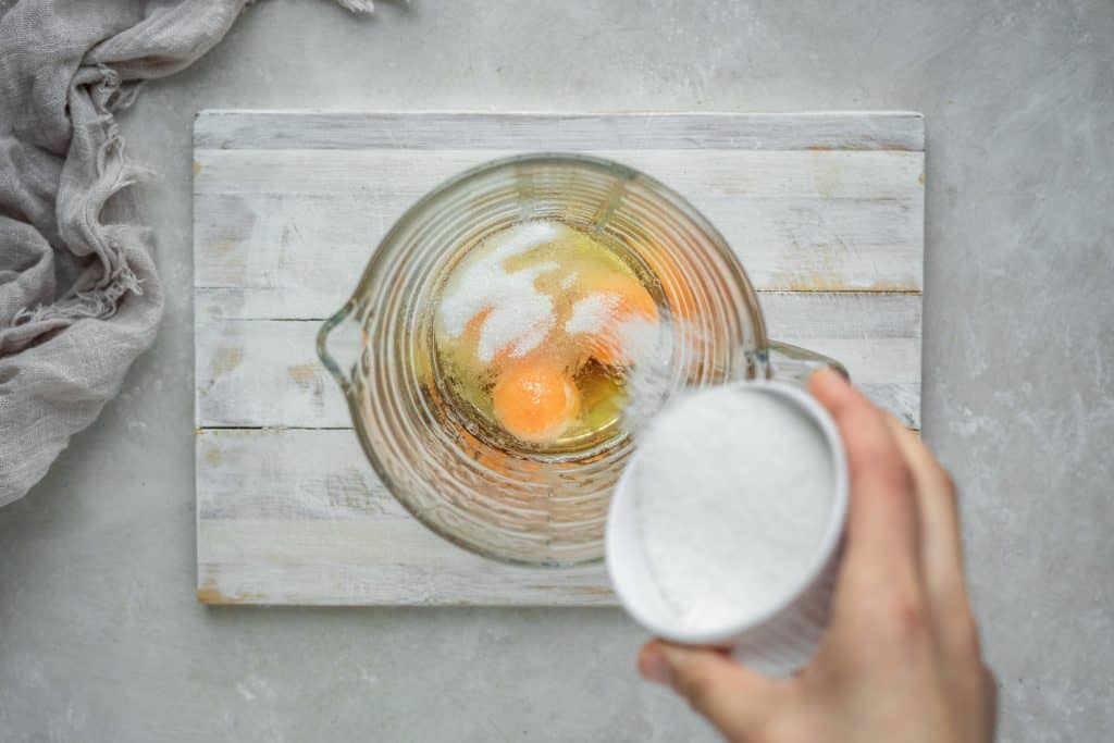 sprinkling sweetener over egg yolks in a bowl