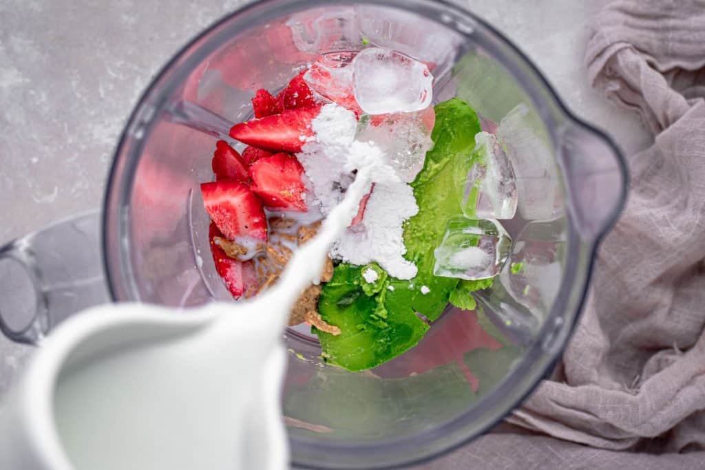 keto strawberry smoothie adding ingredients to a blender before blending the smoothie