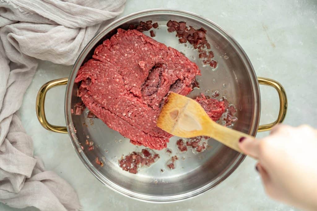 Keto Chili breaking apart ground beef to cook with a wooden spoon