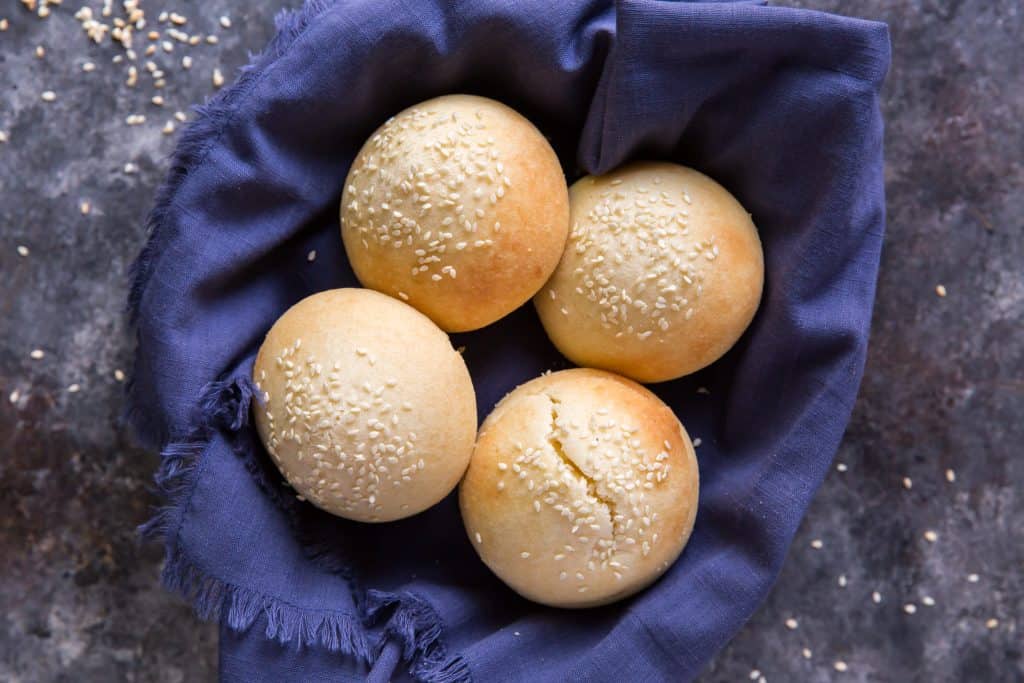 Keto Hamburger Buns A bread basket lined with a blue cloth. It's filled with fresh hamburger buns.