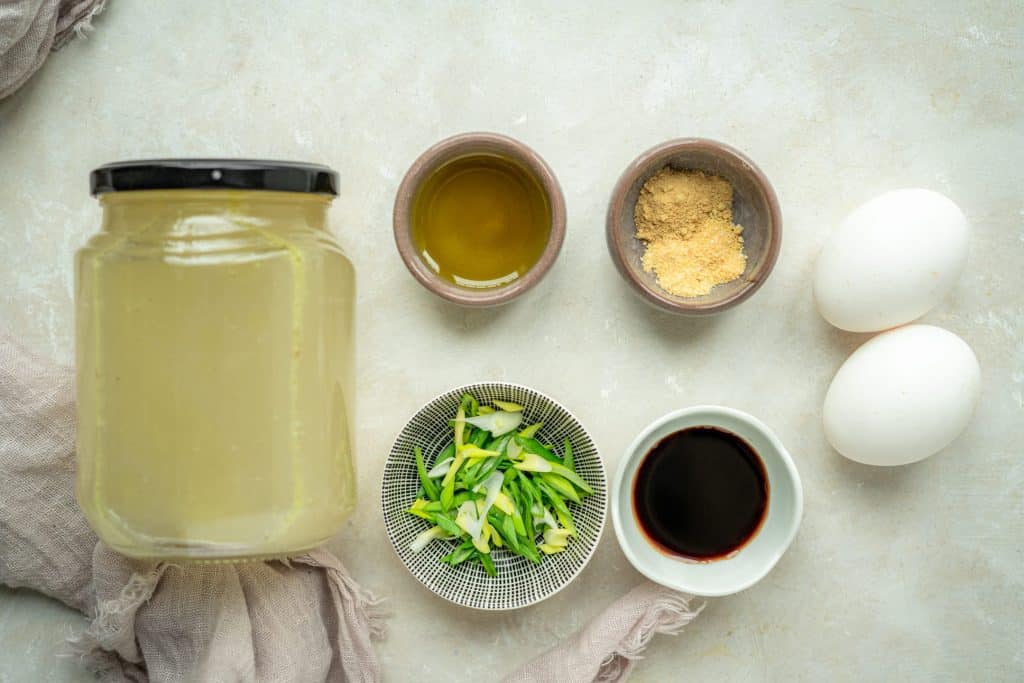 Keto Egg Drop Soup two eggs, chicken broth, spices, and garnishes on white marble