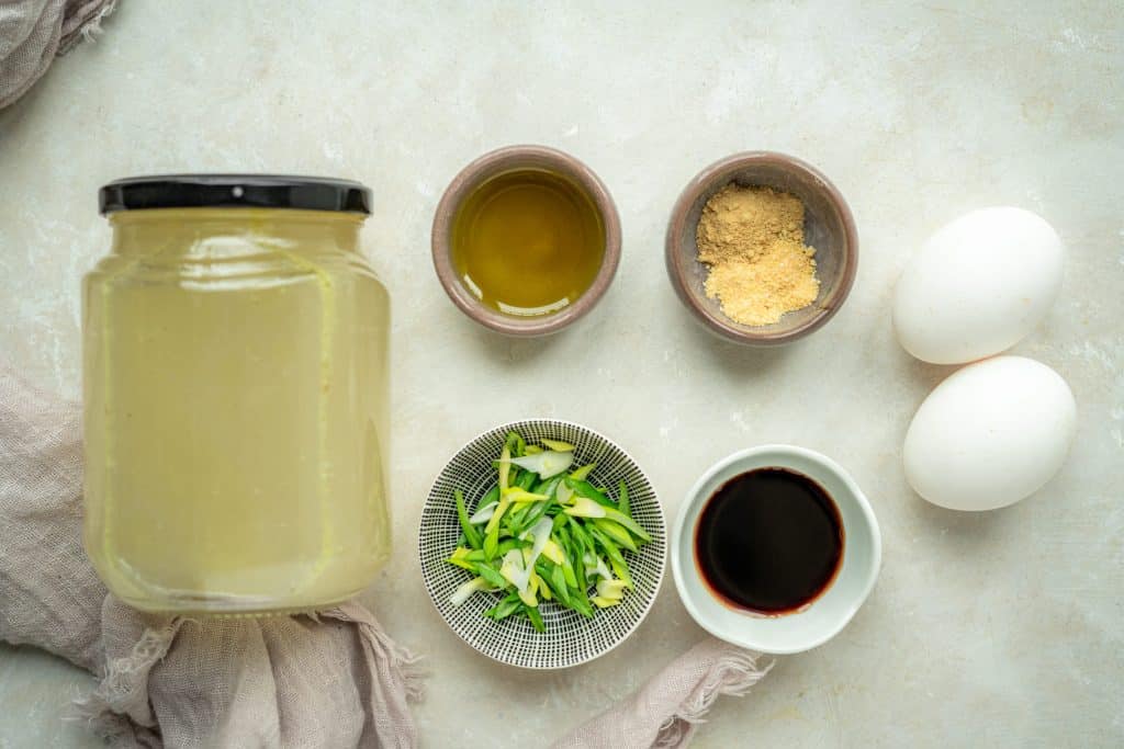 two eggs, chicken broth, spices, and garnishes on white marble