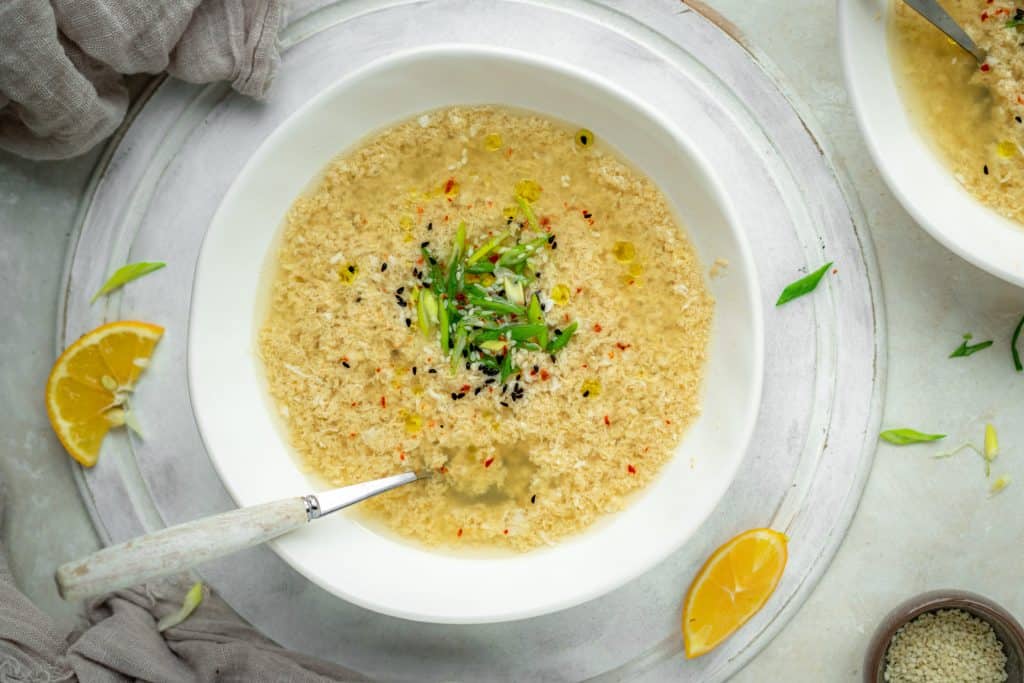 A bowl of egg drop soup center frame by grey cloth and sliced lemon