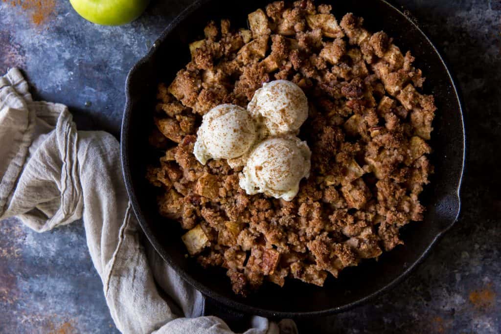 A cast iron pan filled with apple crisp and vanilla ice cream