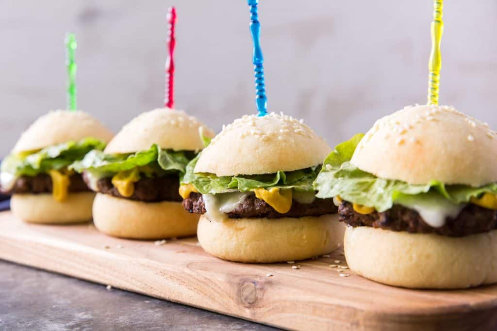 Four sliders on a cutting board sprinkled with sesame seeds