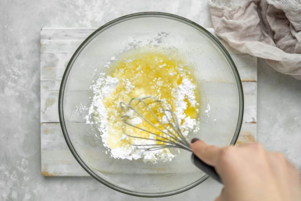 A hand whisking butter and white powdered sweetener together