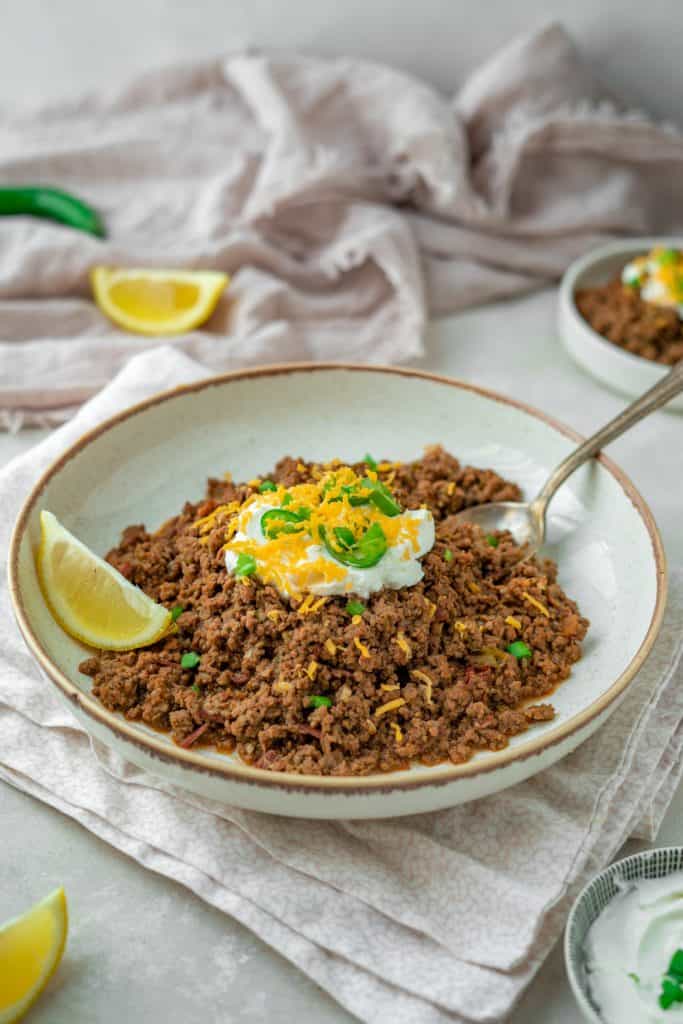 A spoon digging into keto chili topped with cheese and sour cream