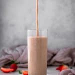 Pouring a glass of strawberry smoothie into a clear tall glass