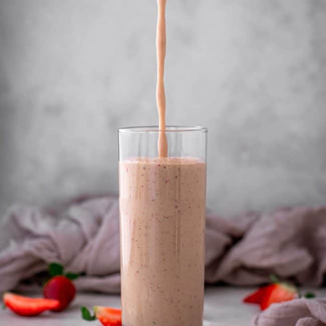 keto strawberry smoothie Pouring a glass of strawberry smoothie into a clear tall glass