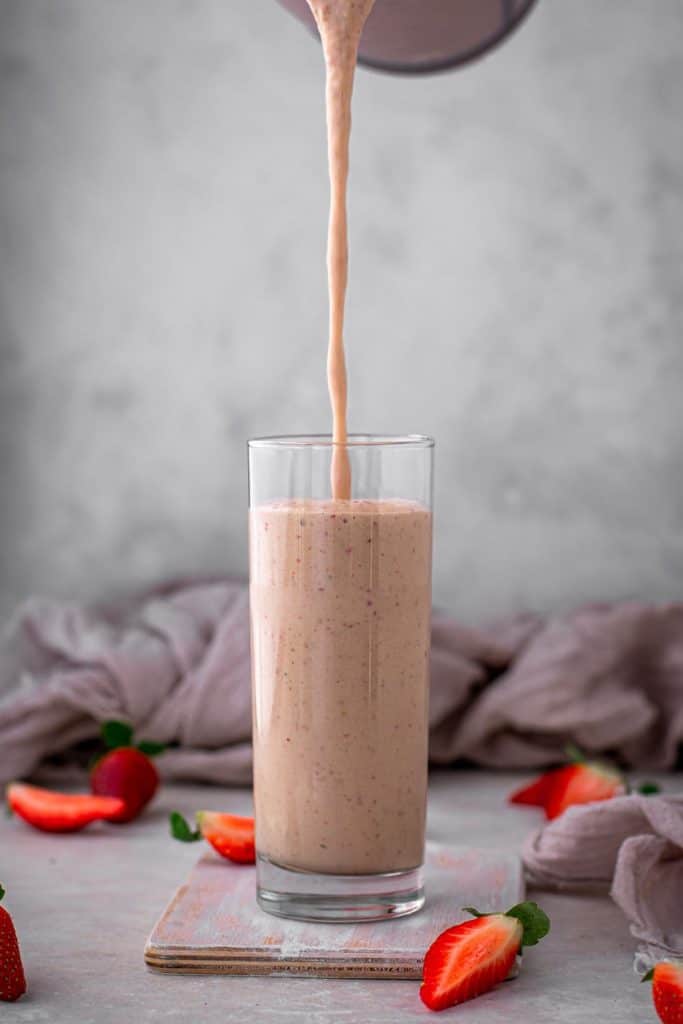 Pouring a glass of strawberry smoothie into a clear tall glass