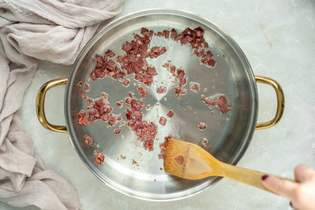 Keto Chili a silver pot with pieces of bacon cooking