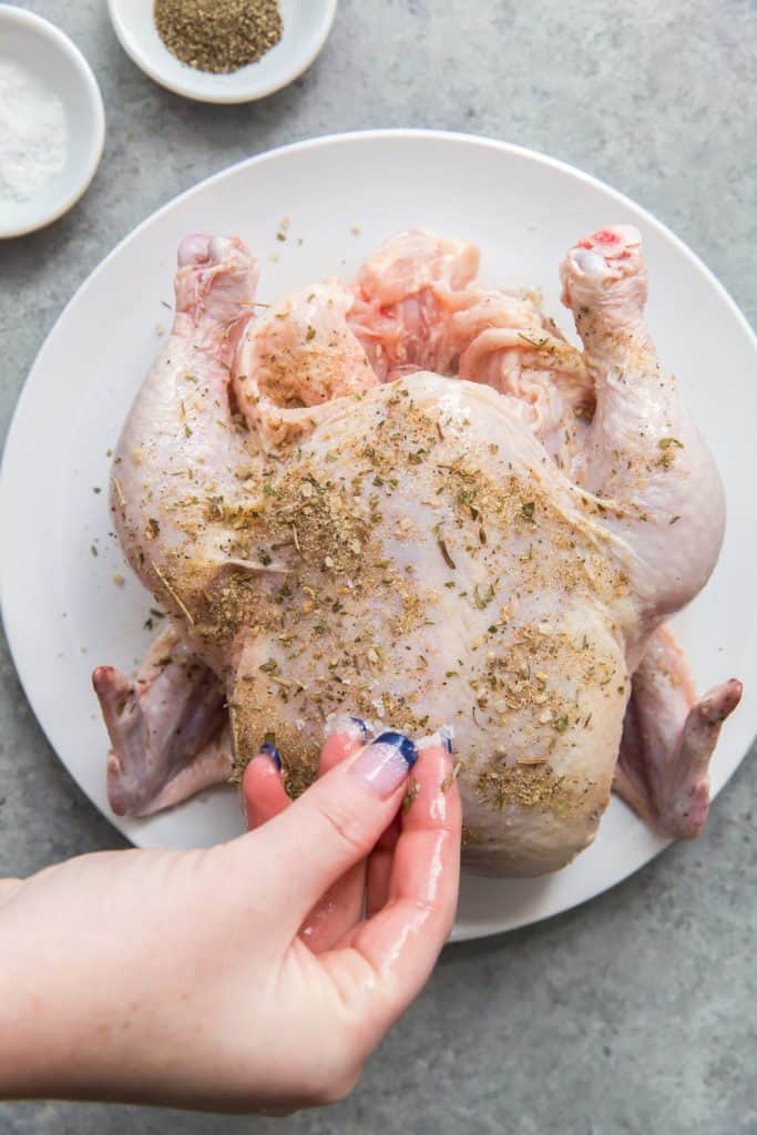 Sprinkling spices on a whole chicken before roasting