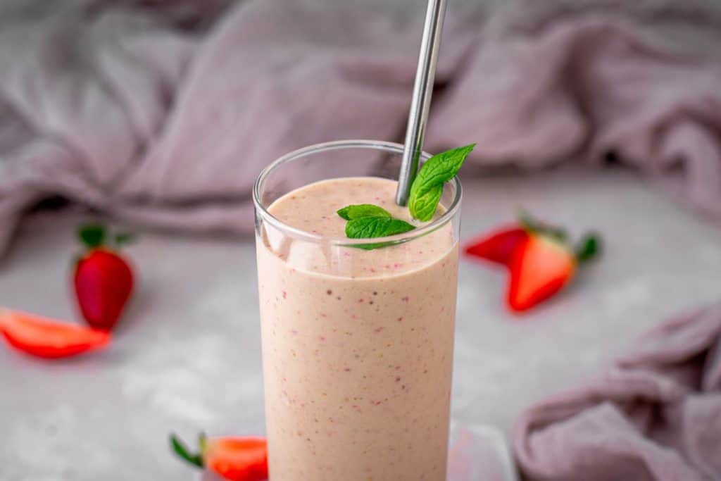 Finished keto strawberry smoothie with mint and sliced strawberries in the background